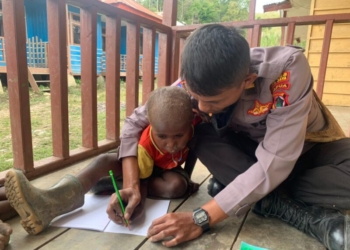 Seorang anggota Polri mengajarkan seorang anak untuk menulis.